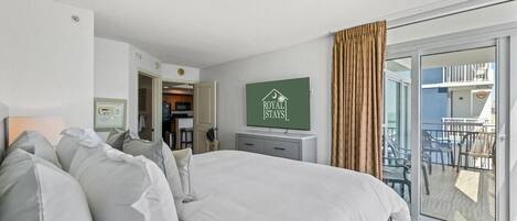 A bedroom with a large bed, a TV mounted on the wall, and a sliding glass door leading to an outdoor area with chairs.