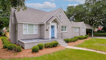 A two-story house with a grey brick exterior, a blue front door, and a small porch with steps.