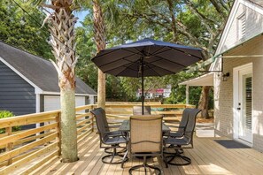 Una terraza de madera con una mesa, sillas, un paraguas y una palmera.