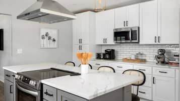A modern kitchen with white cabinets, a stainless steel range, and a central island with a marble countertop.