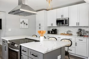 A modern kitchen with white cabinets, a stainless steel range, and a central island with a marble countertop. - Palmetto Grove, Walk to Shem Creek, Mins to Dwt (Mount Pleasant)