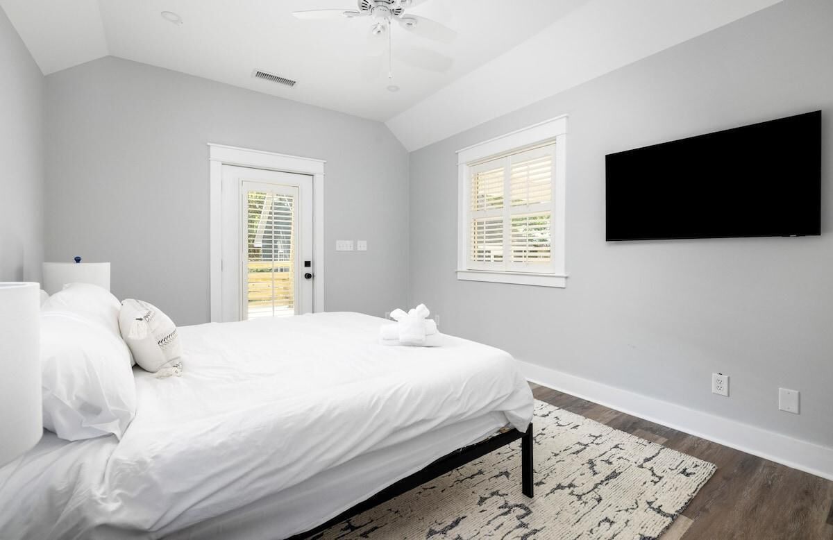 Ein Schlafzimmer mit einem Bett, einem Deckenventilator, einem an der Wand befestigten Fernseher und einem Fenster mit Jalousien.