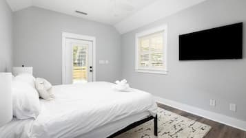 Ein Schlafzimmer mit einem Bett, einem Deckenventilator, einem an der Wand befestigten Fernseher und einem Fenster mit Jalousien.