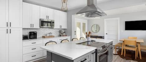 A modern kitchen with white cabinets, a central island, stainless steel appliances, and a dining area with a wooden table and chairs.