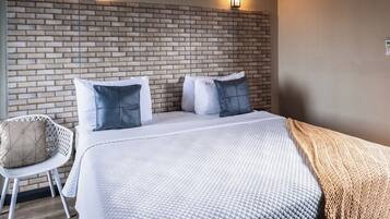 A hotel room with a brick-patterned headboard, a white bed with multiple pillows, a white chair, and a wooden floor.