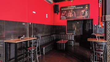 Un restaurante con paredes rojas, con una barra de cuero negro, mesas y sillas.