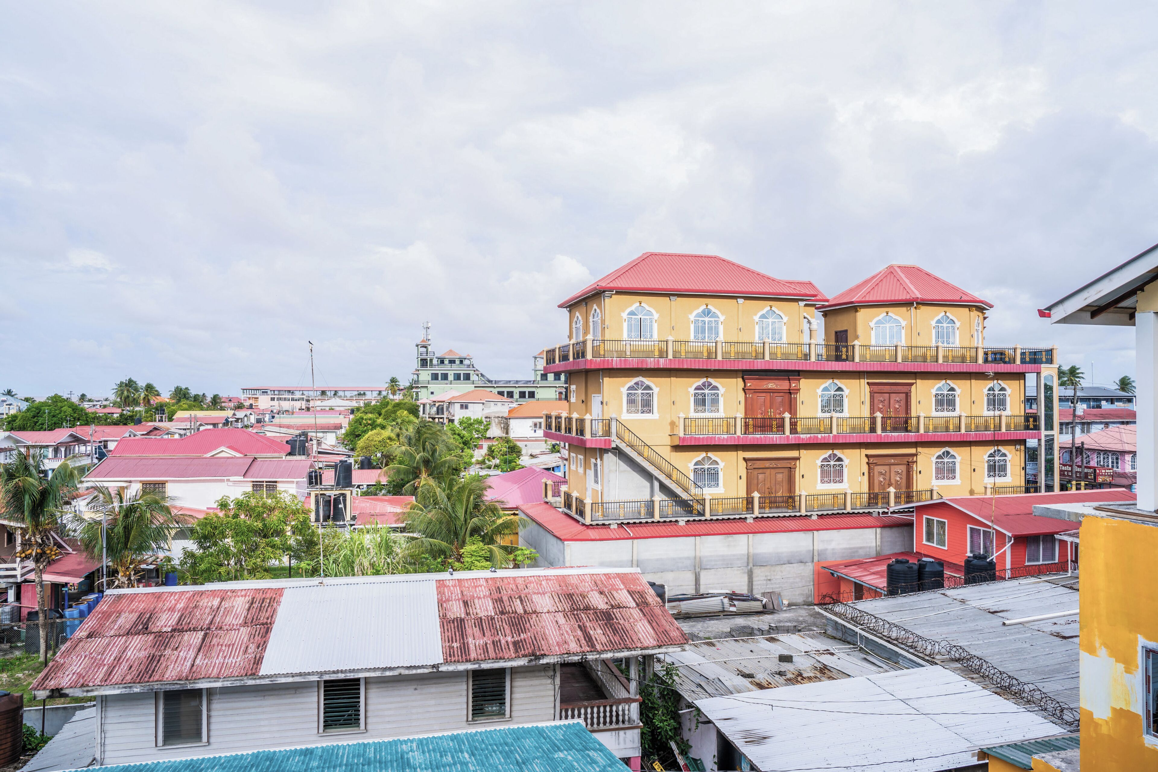 Um edifício de vários andares com telhado vermelho, varandas e fachada amarela marcante.