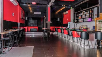 A bar area with red and black decor, bar stools, and a counter with various bottles.
