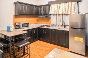 A compact kitchen with dark cabinets, a microwave, a gas stove, and a refrigerator. - Shelbees Suites (Cornelia Ida)