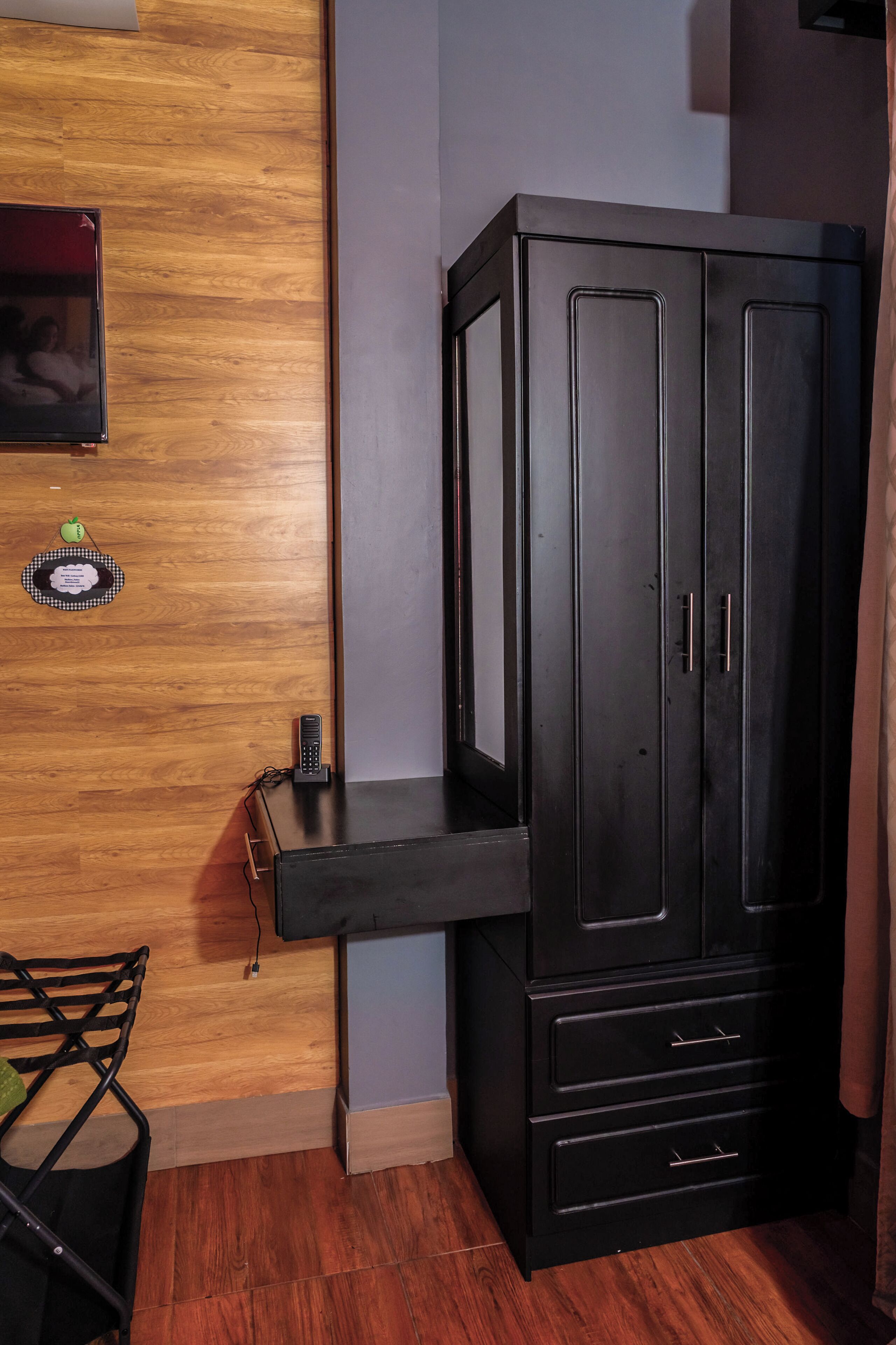 A room with a wooden floor, a black cabinet with drawers, a small table, and a chair.