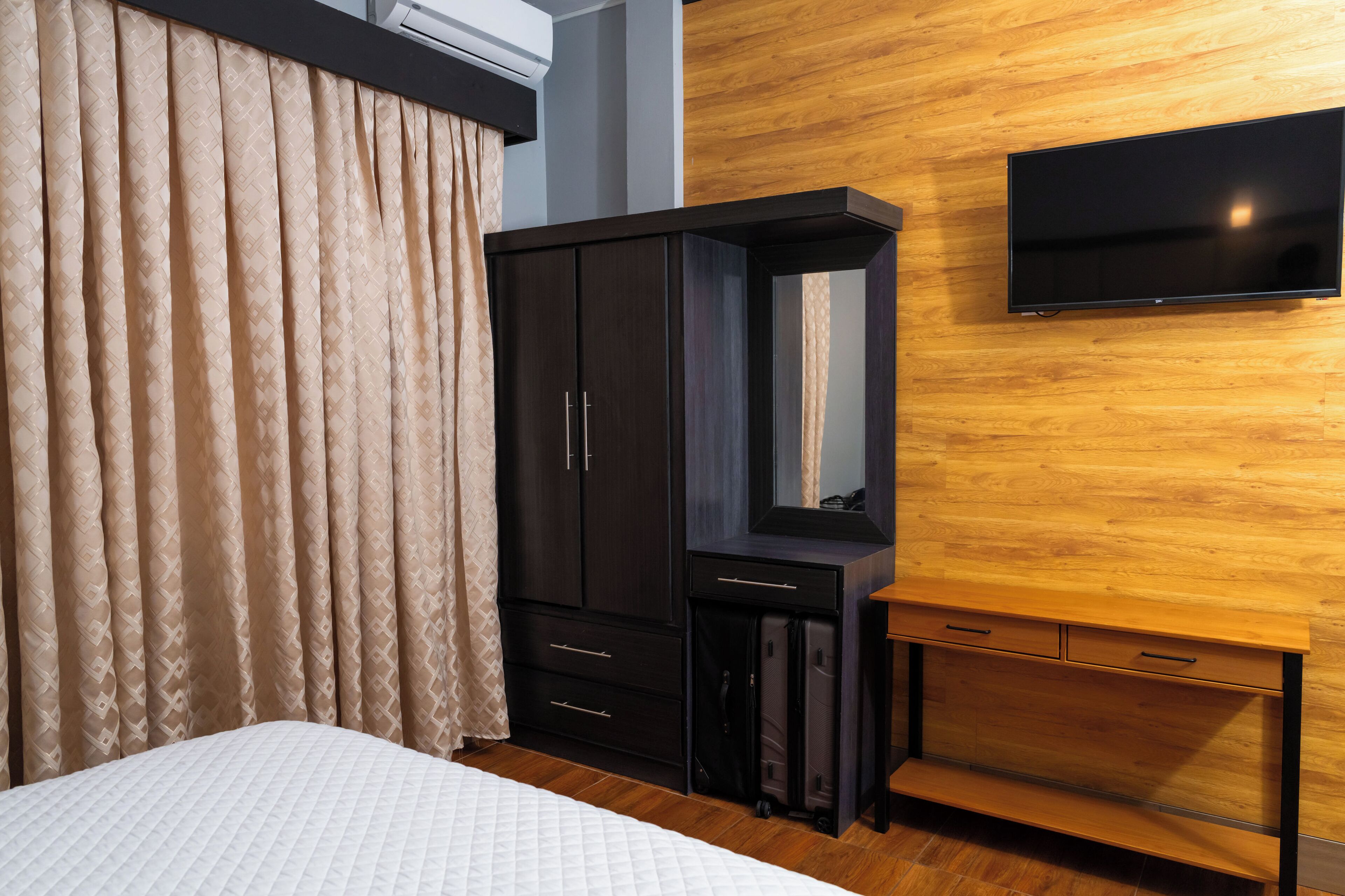 A hotel room with a bed, a wardrobe, a mirror, and a television mounted on the wall.