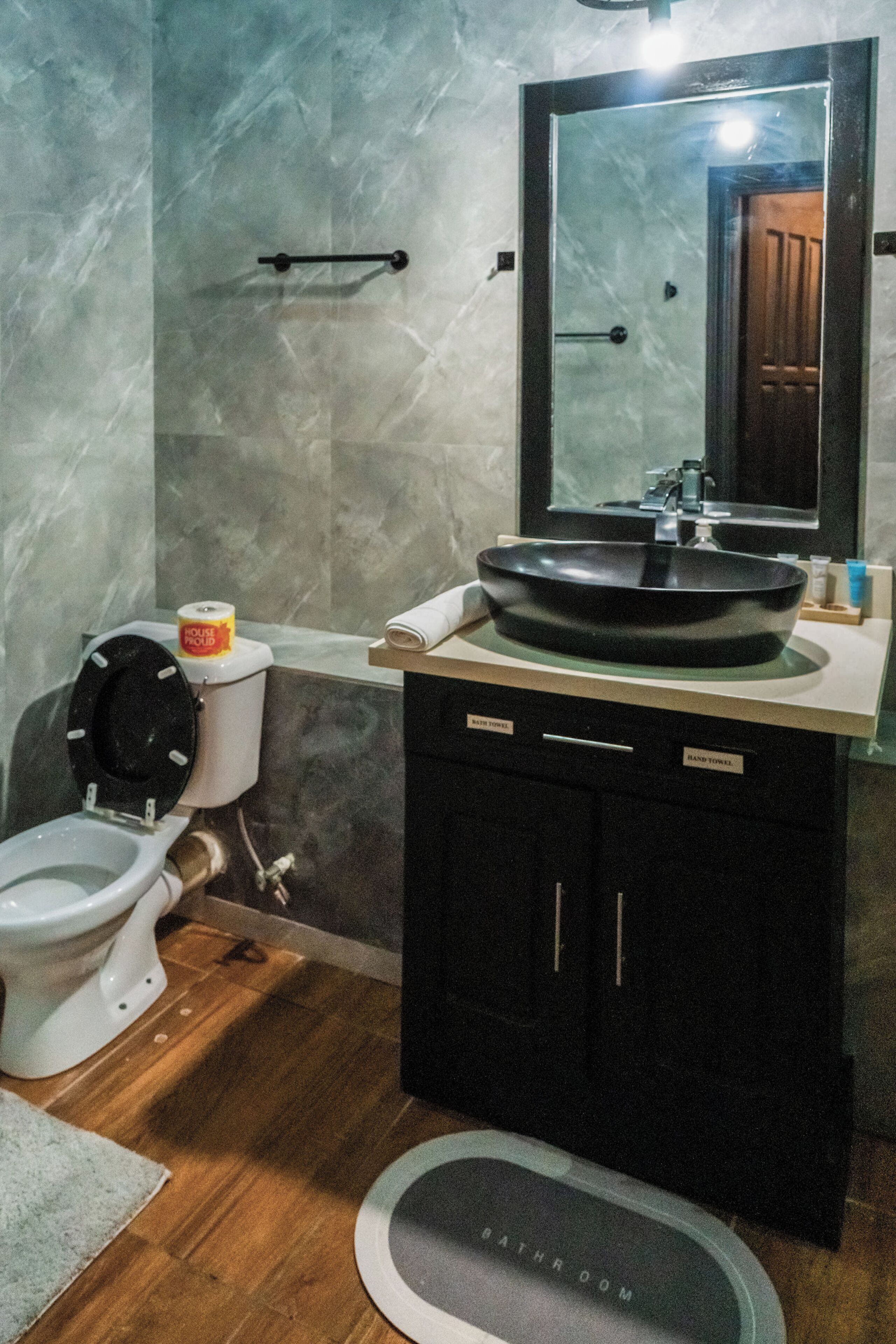 A bathroom with a toilet, sink, mirror, and a hand towel dispenser.