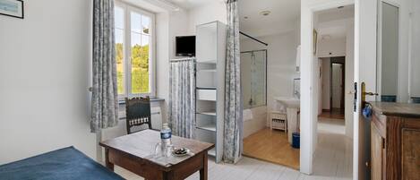 A room with a bed, a table with a bottle, a TV, and a shower area.