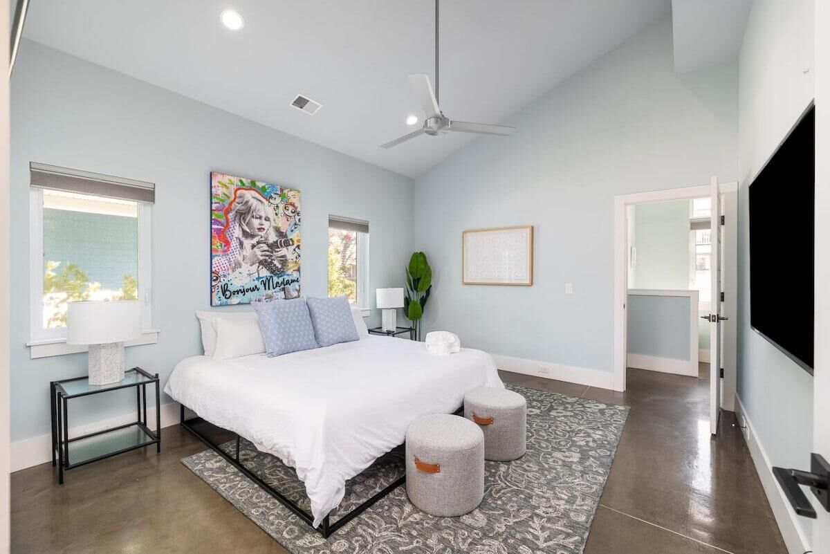 A modern bedroom with a bed, bedside tables, a ceiling fan, a large window, and a door leading to another room.