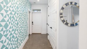 A hallway with a geometric patterned wall, a white door, and a round mirror with a striped frame. - The Polygon, Park Circle, Pet Friendly (North Charleston)