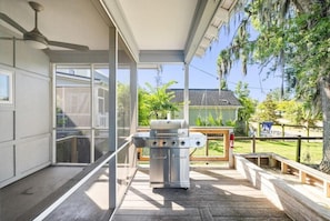 Un espacio al aire libre techado con una parrilla de acero inoxidable, un ventilador de techo y vista a una casa y árboles.