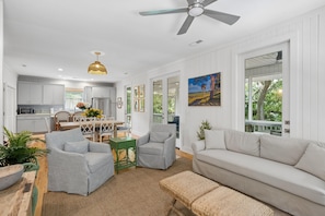 A modern living room with a sofa, chairs, a dining table, and a kitchen in the background. - Chasing Waves Heated Pool 3 Min Beach (Edisto Island)