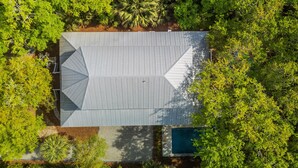 Vista aérea de una casa con techo inclinado, rodeada de abundante vegetación y una piscina.