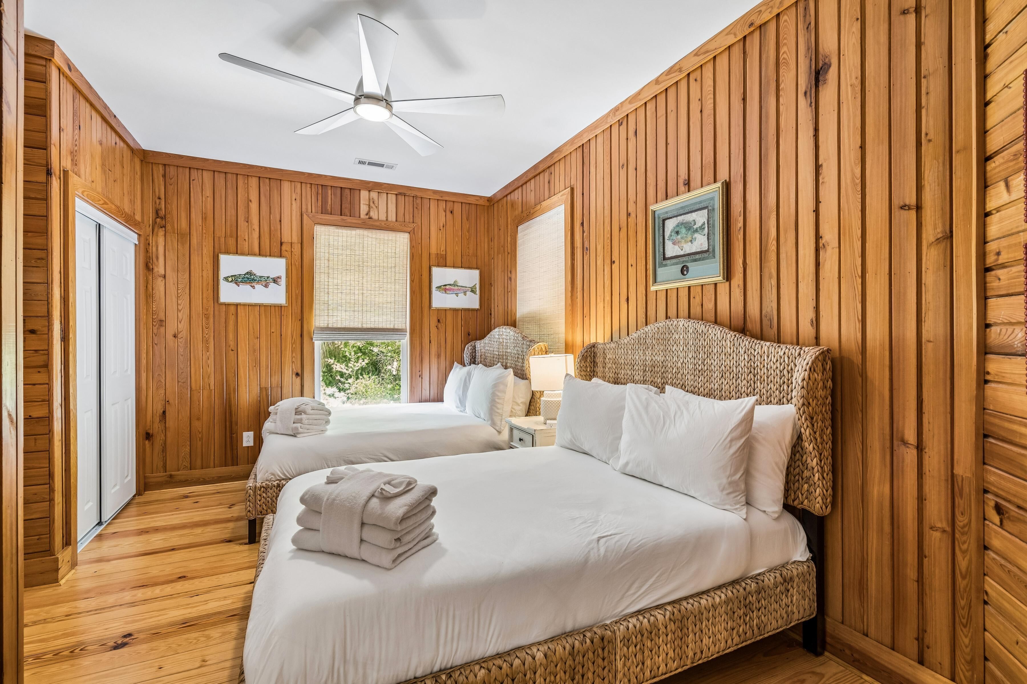 Quarto com painéis de madeira, duas camas, um ventilador de teto e quadros nas paredes.