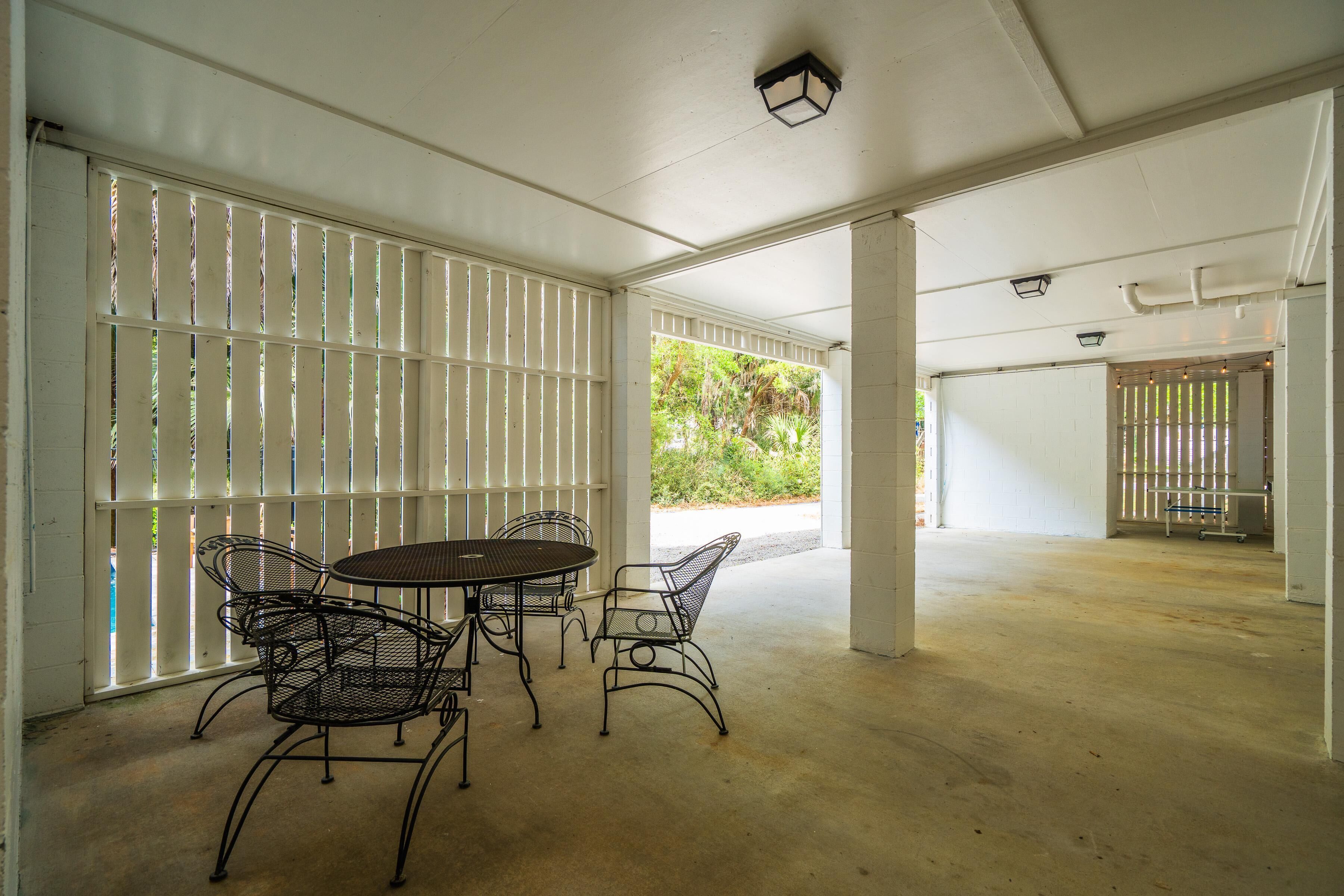 A covered outdoor area with a table and chairs, a concrete floor, and a view of greenery outside.