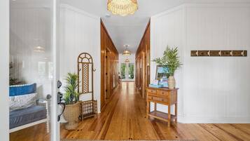 A hallway with wooden flooring, a wicker lamp, a wooden console table with plants, and a decorative wall piece.