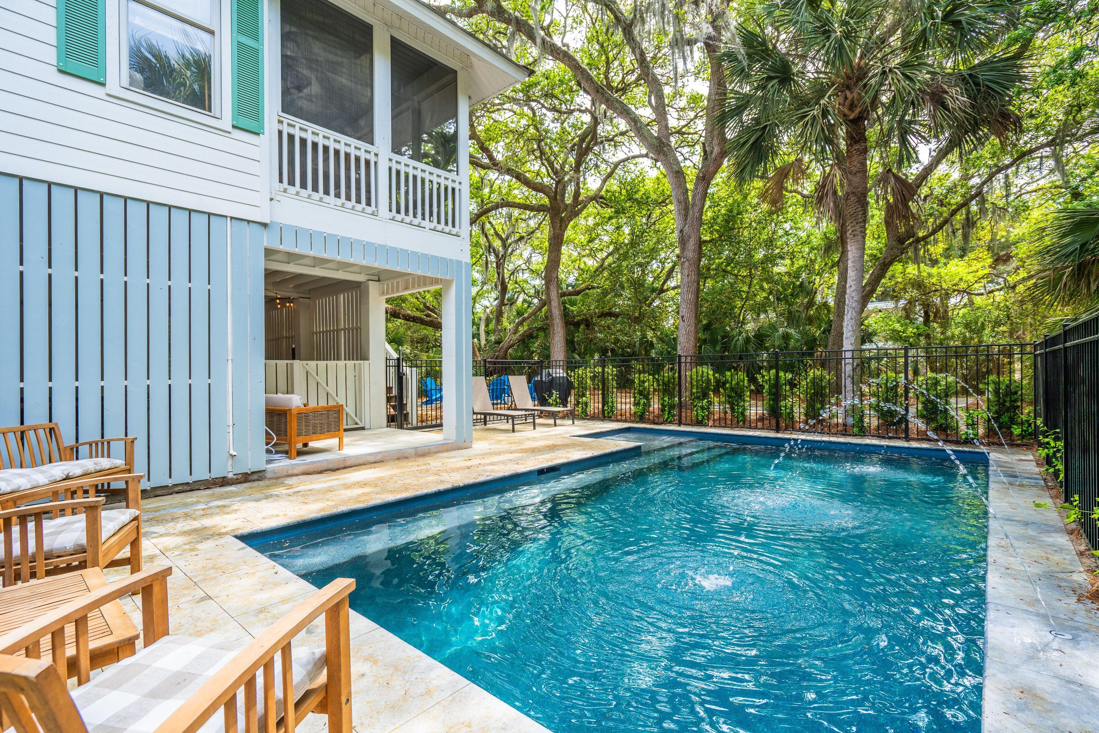 Piscina com deck de madeira e cadeiras de descanso, cercada por árvores e um espaço delimitado por cerca.