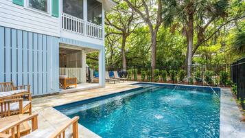 Piscina com deck de madeira e cadeiras de descanso, cercada por árvores e um espaço delimitado por cerca.