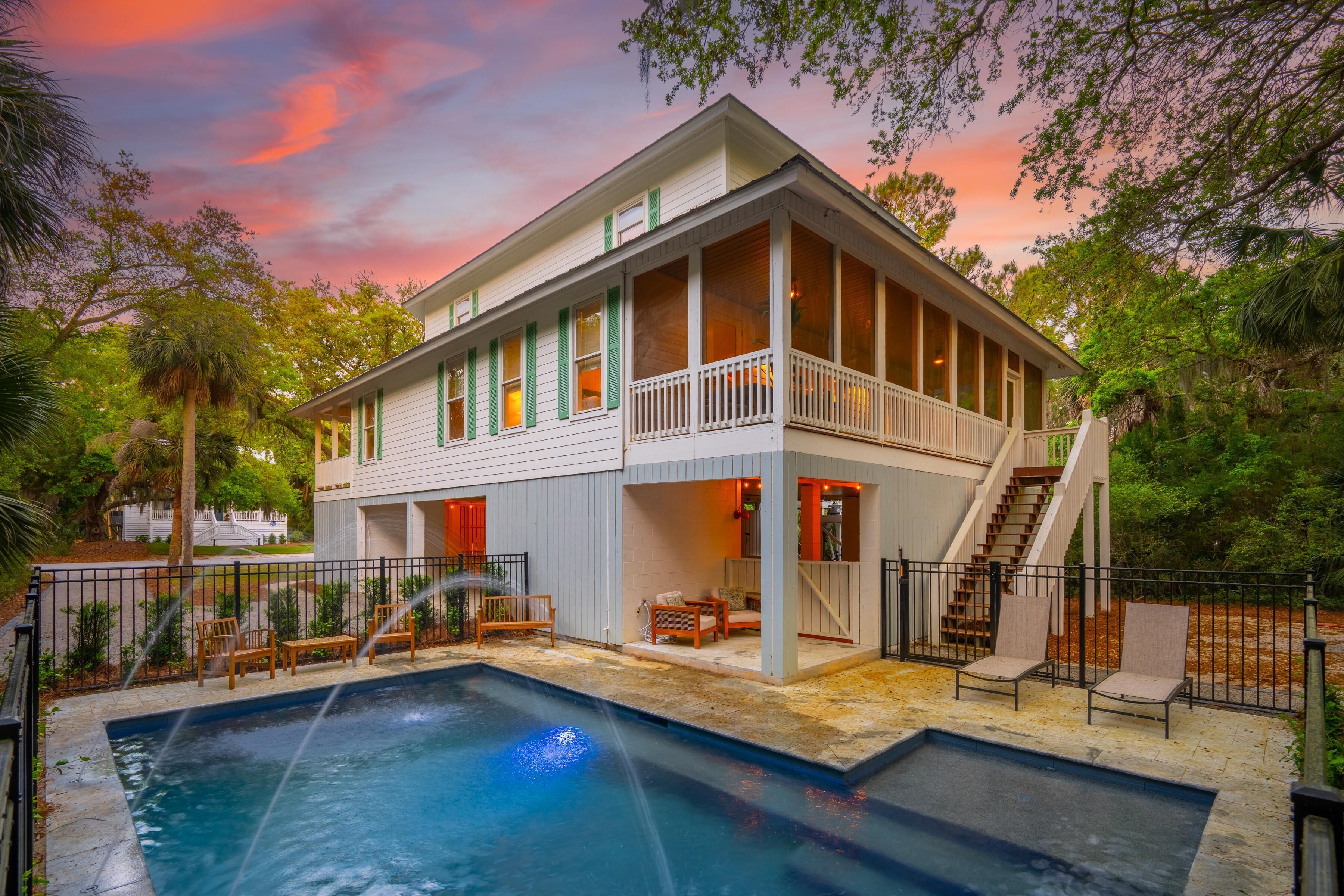 A two-story house with a pool, outdoor seating, and a staircase leading to a balcony.