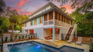 A two-story house with a pool, outdoor seating, and a staircase leading to a balcony.