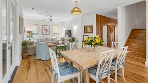 Amplia sala de estar con una mesa de comedor de madera, sillas blancas y una escalera.