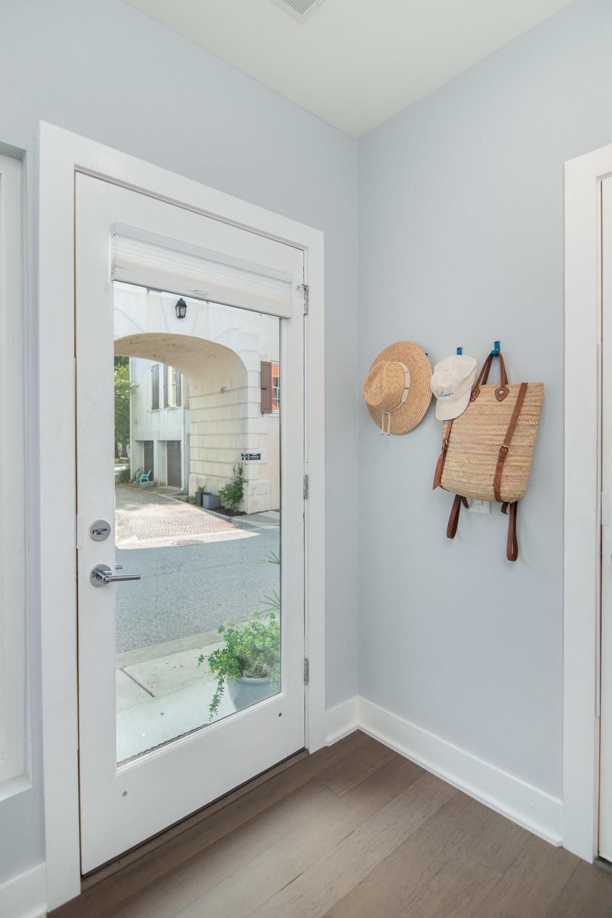 Una porta bianca con un pannello di vetro, un corridoio con pareti grigio chiaro e un pavimento in legno.