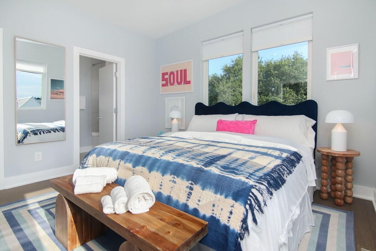 A bedroom with a bed, a bedside table with towels, a mirror, a wall with a 'SOUL' sign, and a window with a view of trees.