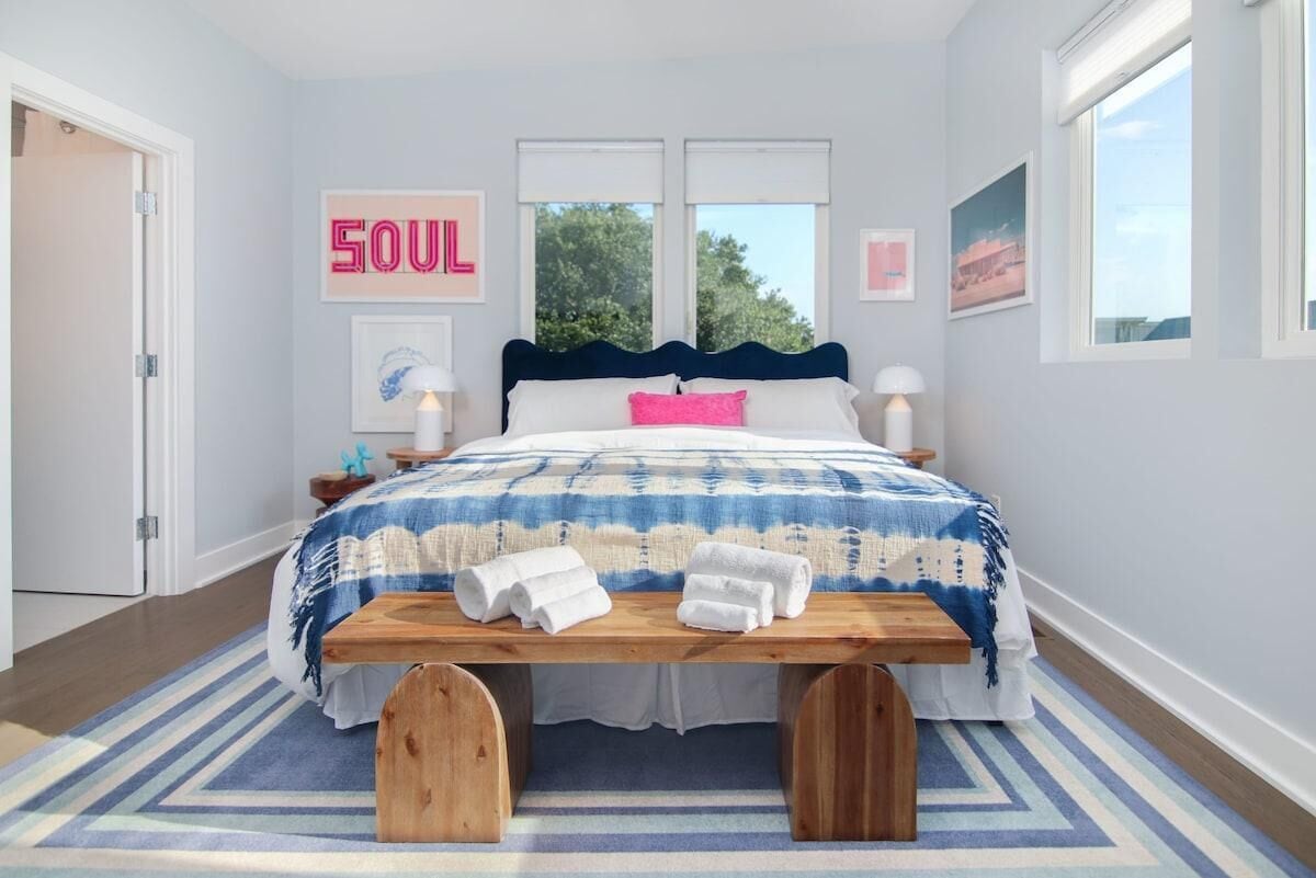 A bedroom with a bed, a bedside table, a bench, a rug, and a wall with a sign.