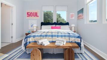 A bedroom with a bed, a bedside table, a bench, a rug, and a wall with a sign.