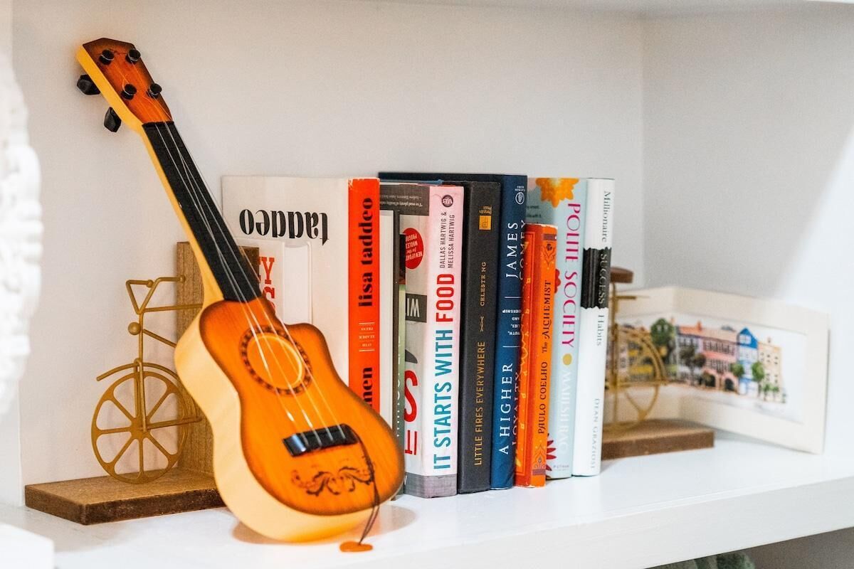Una estantería con una guitarra, libros y un adorno pequeño.