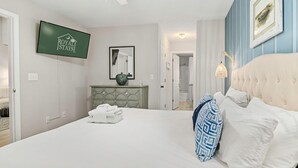 Habitación de hotel con una cama, televisión, espejo, cómoda y puerta que da a un baño.