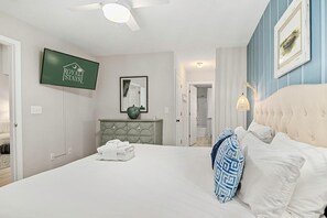 Habitación de hotel con una cama, televisión, espejo, cómoda y puerta que da a un baño.