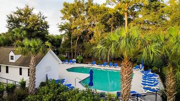 A swimming pool with blue lounge chairs, surrounded by palm trees and other greenery.