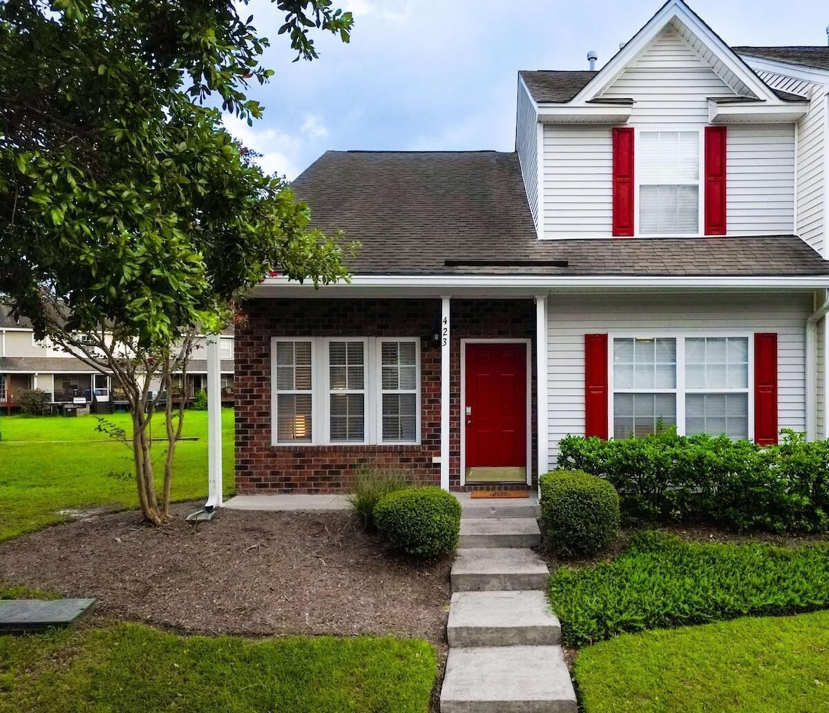 A two-story house with a red door, white shutters, and a brick section.