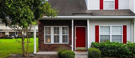 A two-story house with a red door, white shutters, and a brick section.