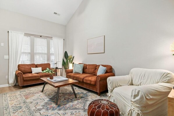 Una sala de estar con dos sofás de cuero marrón, un sillón blanco, una mesa de centro de madera y un tapete estampado.