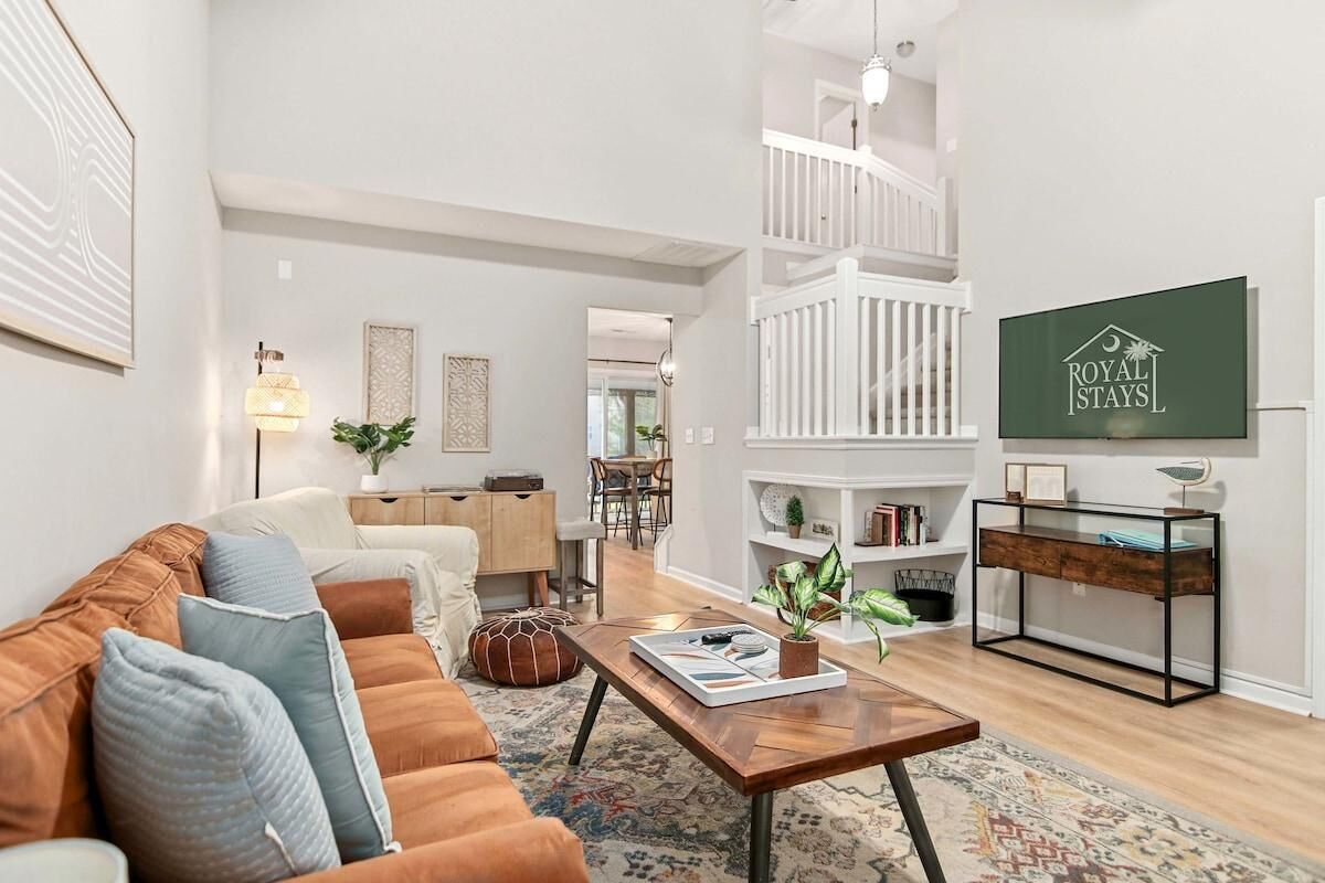 A spacious living room with a brown sofa, a coffee table, and a staircase leading to a loft area.