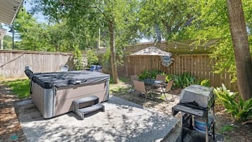 A backyard with a hot tub, a grill, and a table with chairs.