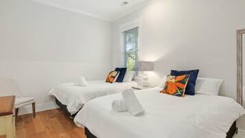 A hotel room with two beds, white bedding, and colorful pillows. There is a chair and a small table in the corner.