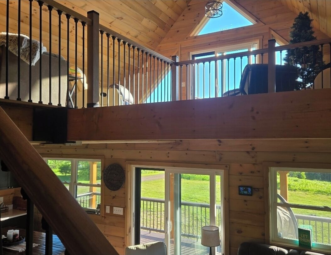 A wooden cabin with a loft bedroom, a dining area, and a view of a green landscape.