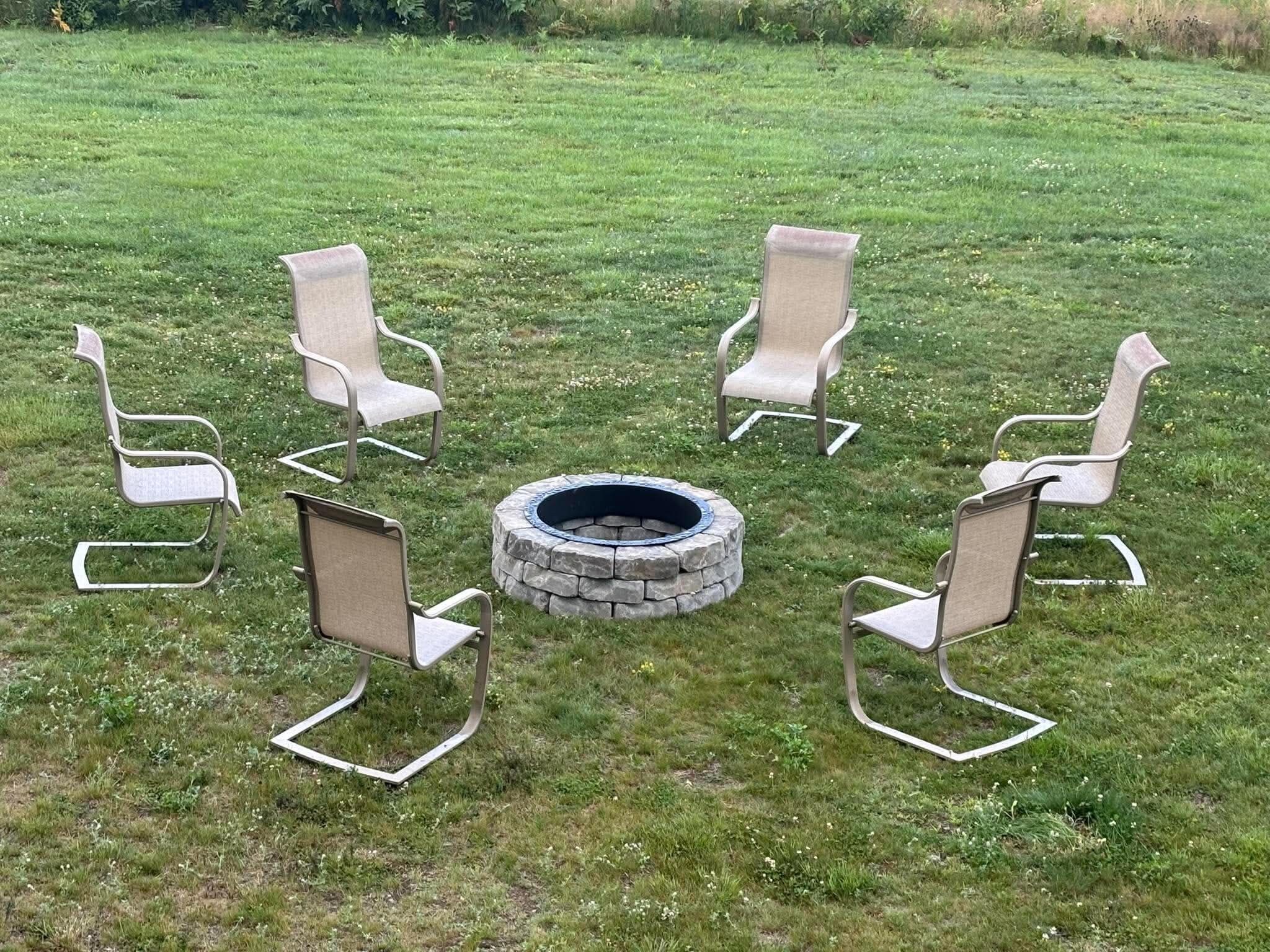 A circular arrangement of chairs around a stone fire pit in an outdoor grassy area.