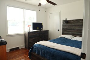 Un dormitorio con cama, cómoda, televisor y ventilador de techo.
