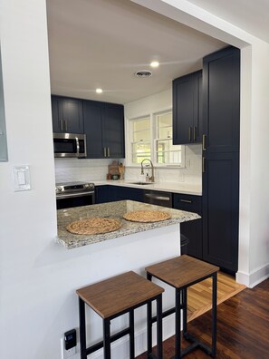 A modern kitchen with dark cabinets, granite countertops, a built-in microwave, and a small wooden table.