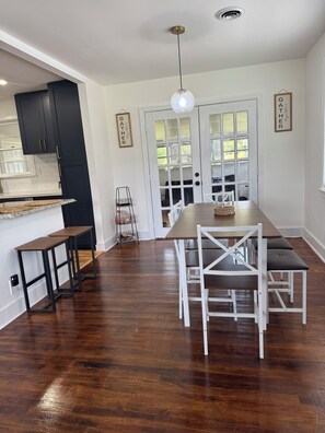 A modern kitchen with dark cabinets, a wooden countertop, and a dining area with a wooden table and white chairs.