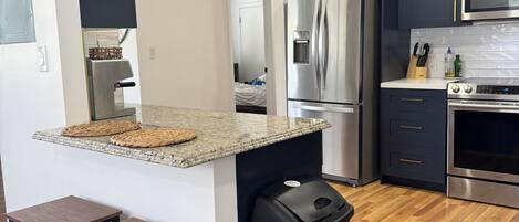 A modern kitchen with dark cabinets, stainless steel appliances, a granite countertop, and wooden flooring.